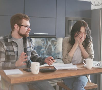 A couple in a kitchen discussing financial problems with visible frustration and worry.